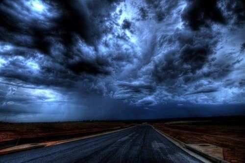 Dramatic storm clouds over an empty road, creating a gloomy atmosphere.